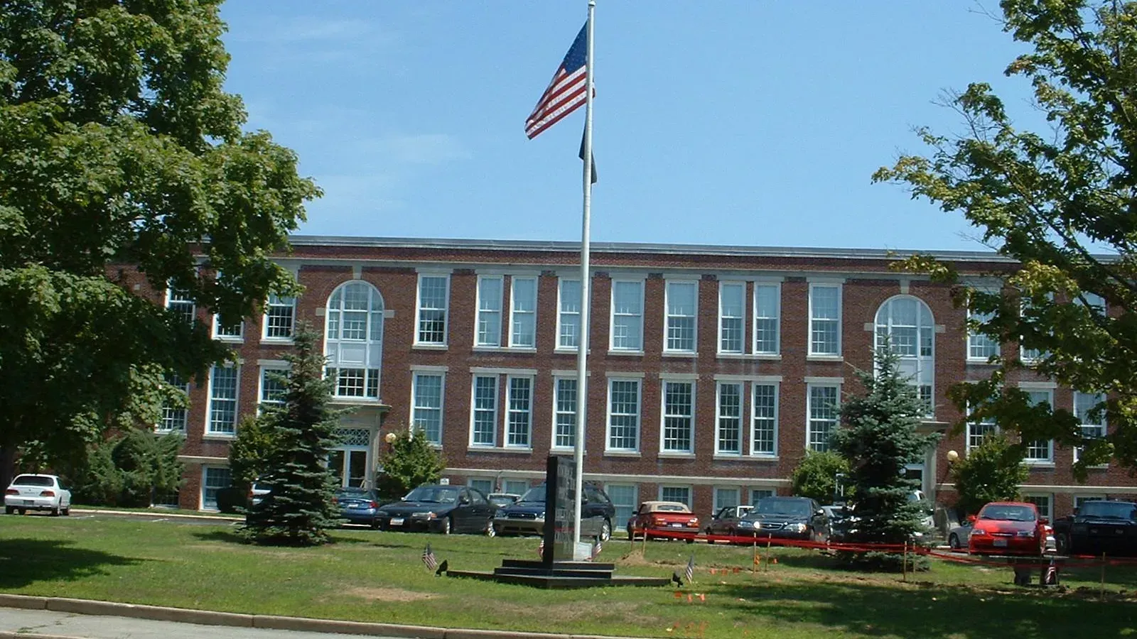 Dartmouth Town Hall, a long three-story brick building with arched windows behind a flagpole and front lawn, Dartmouth, Massachusetts