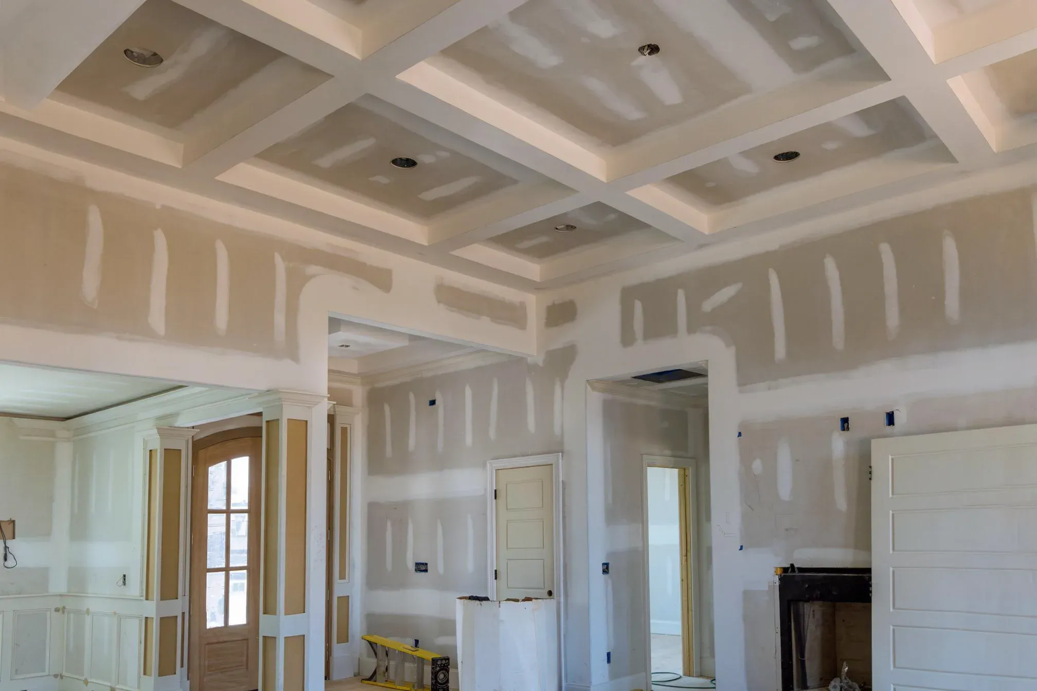 Interior with a coffered drywall ceiling and taped, mudded walls, doorway openings and a bare firebox, unpainted before finishing
