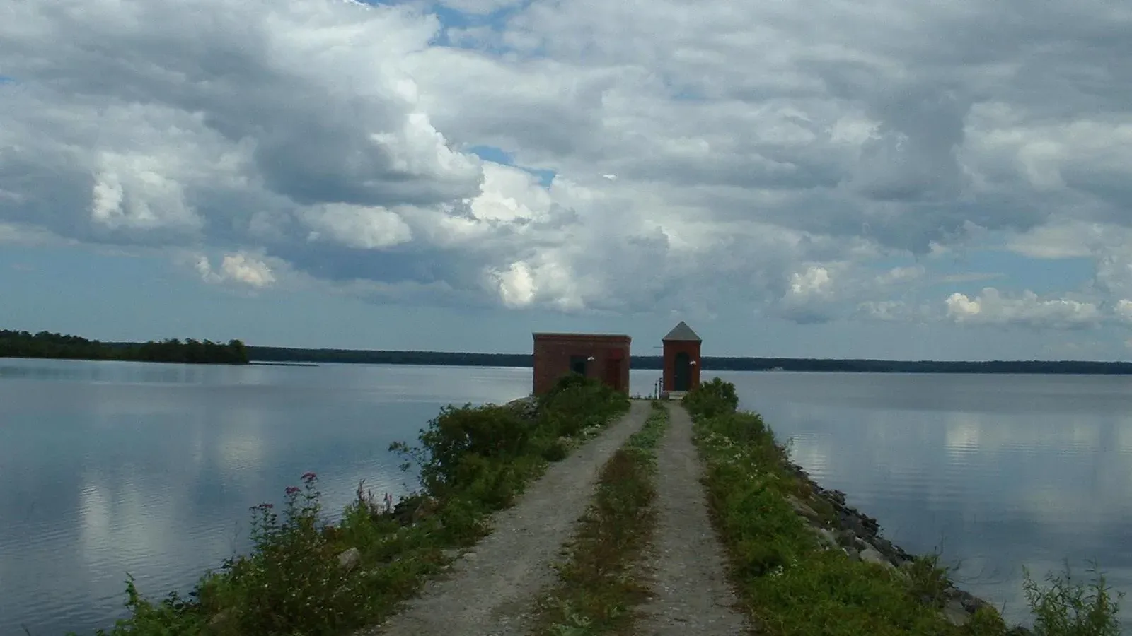 A stone causeway leading to a small brick pump house on Assawompset Pond under a cloudy sky, Lakeville, Massachusetts