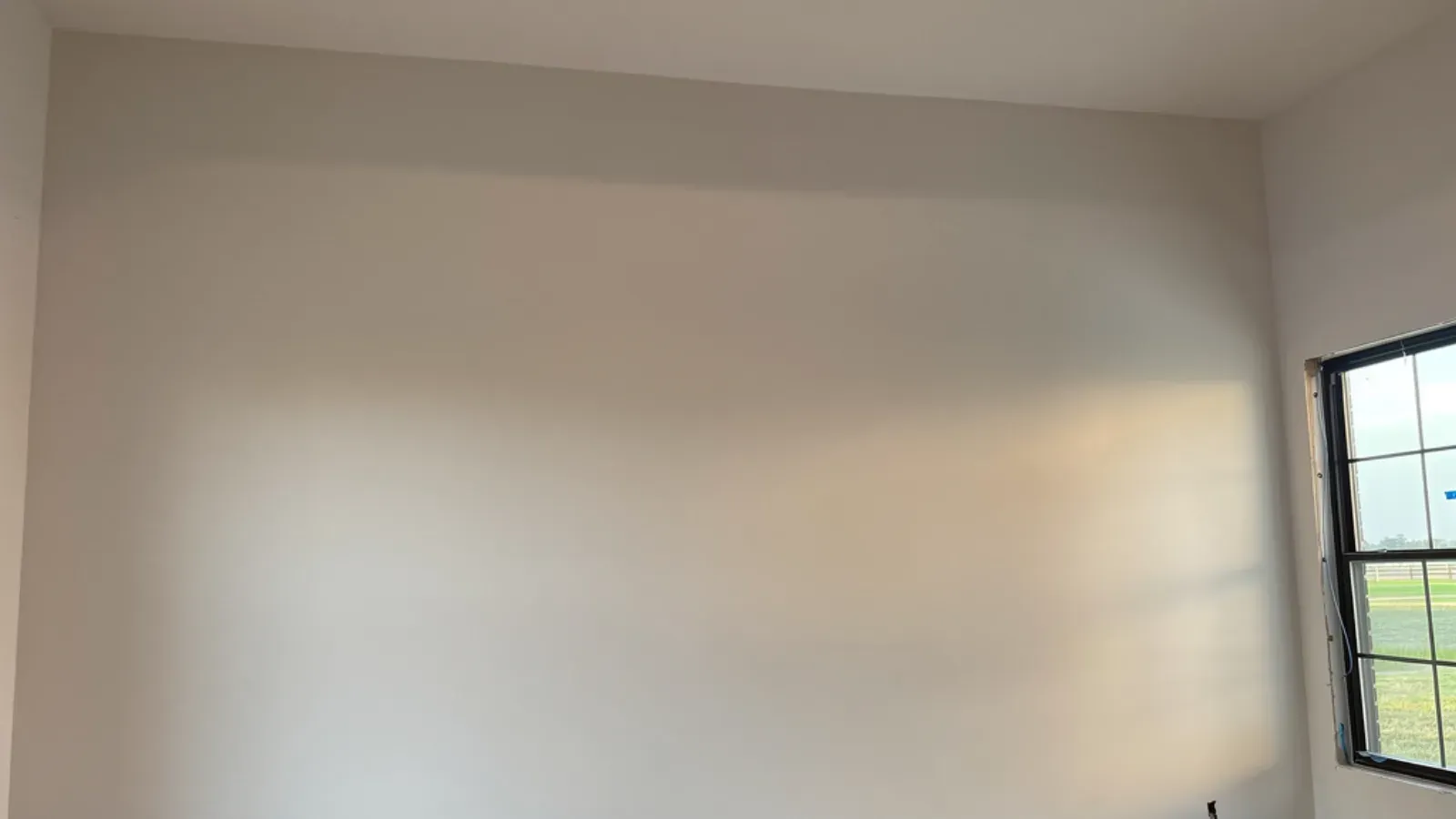 A wall skim-coated to a smooth, even off-white finish, with daylight raking across it from a side window